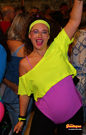 Chica de los 80s con leggings negros, top amarillo fosforito y vestido violeta cantando en El Gran Guateque